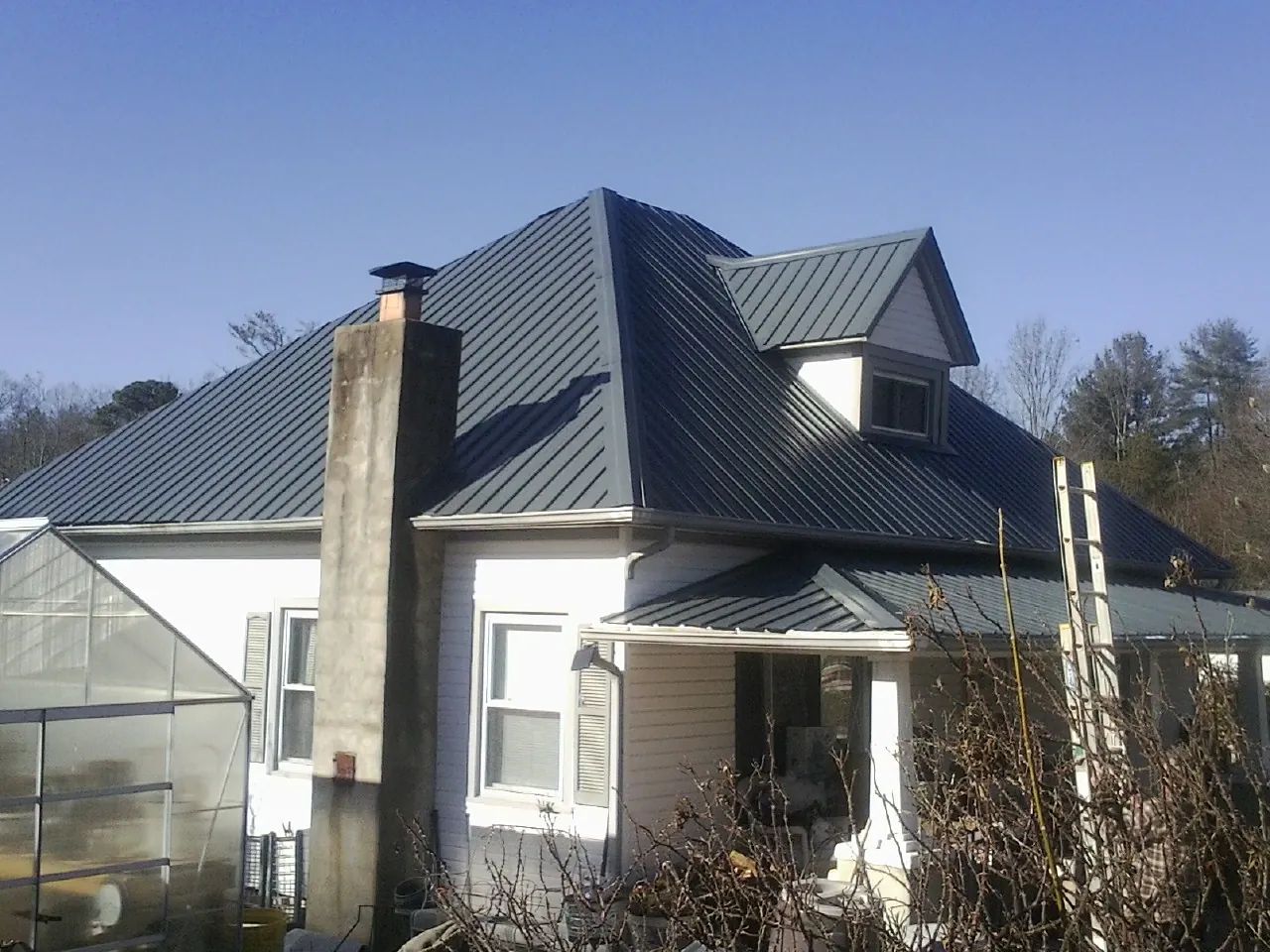 Dark blue standing seam metal roof on a white farmhouse with dormer — Slate & Tile Roof Repair by Roofing Brothers in Stroh