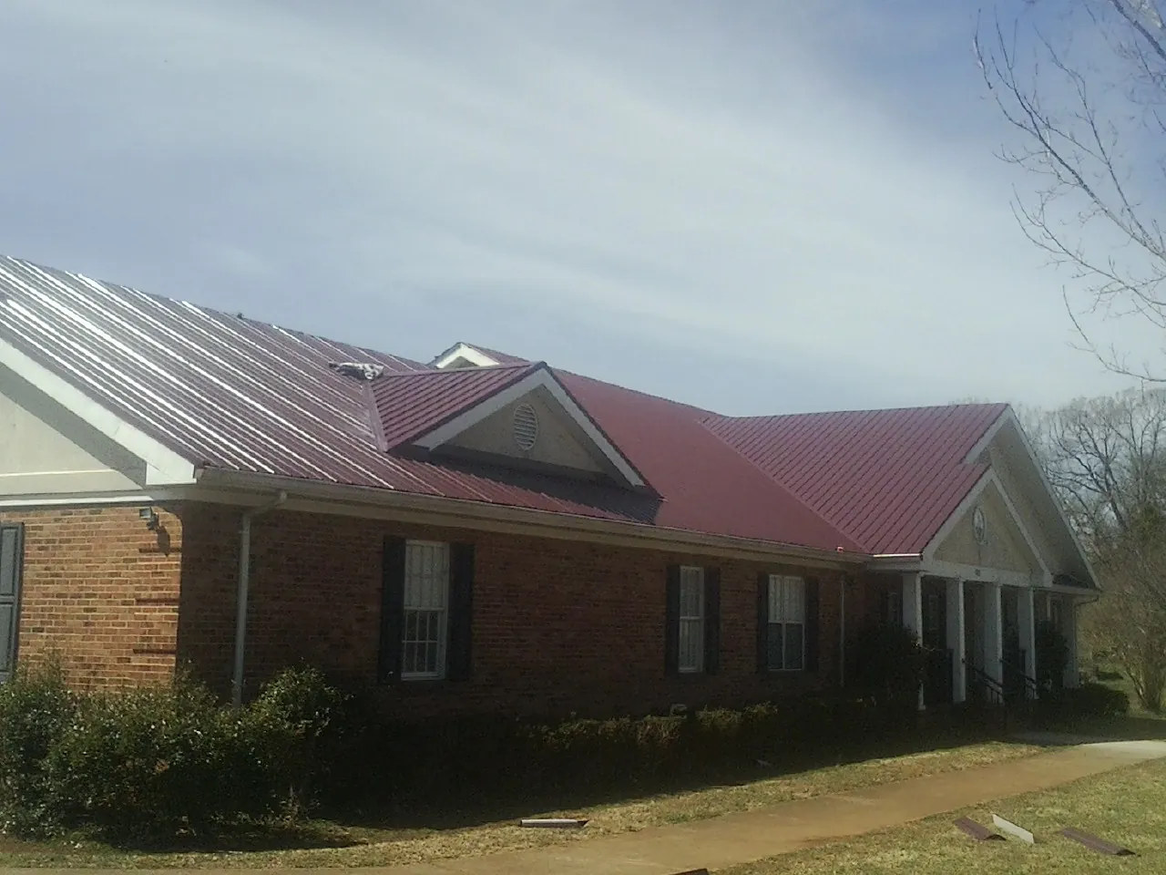 Red metal roof with gabled entries on a long brick building, from a Hail Damage Roof Repair job in Stroh