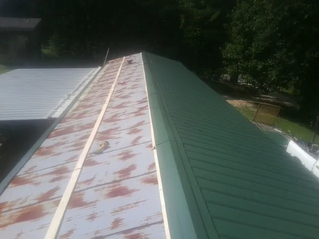 Old rusted panels beside newly installed green metal roofing — Wind Damage Roof Repair by Roofing Brothers in Stroh