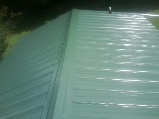 New green metal panels meeting at the ridge of a roof — Flat Roof Repair work by our crew in Stroh