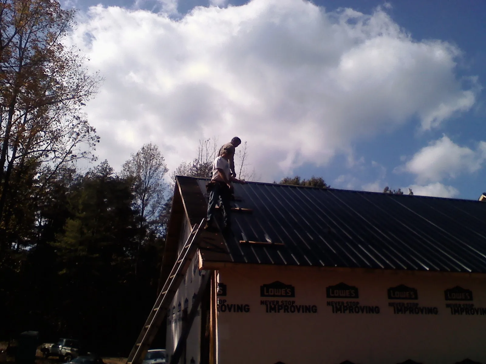 Roofer fastening dark metal panels high against a cloudy sky, from a Roof Inspection job in Stroh